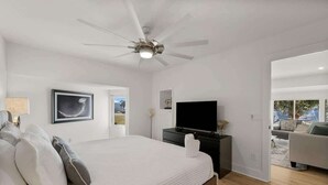 Un dormitorio con cama, ventilador de techo, televisión y vistas al exterior.