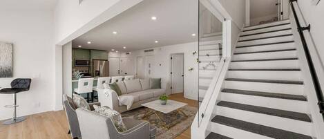 A modern living room with a sofa, chairs, and a coffee table. There is a staircase with a railing leading to an upper floor.