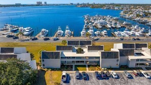 Un puerto deportivo con varias embarcaciones amarradas, un estacionamiento con varios coches y un edificio moderno de techo plano.