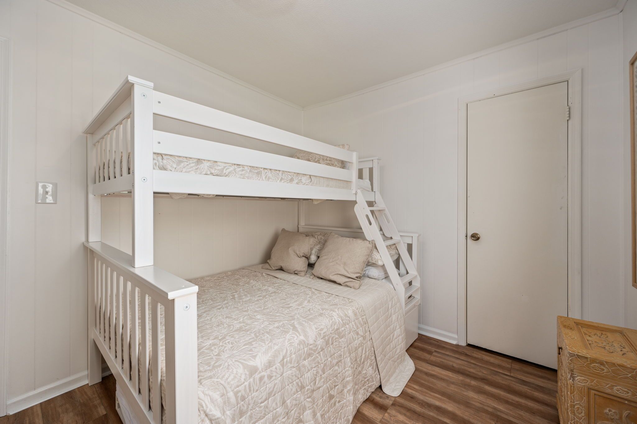 A bunk bed with a ladder, a door, and a wooden chest of drawers.