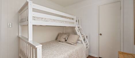 A bunk bed with a ladder, a door, and a wooden chest of drawers.