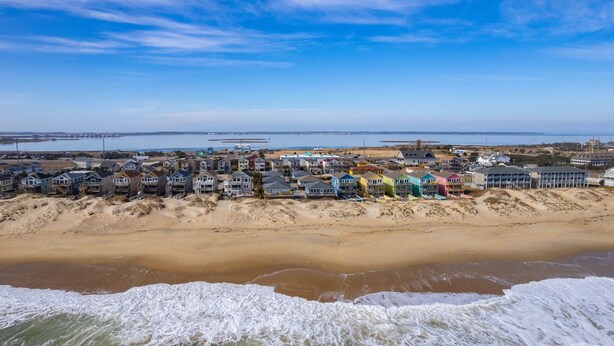 A coastal residential area with houses along the beach, a pier in the background, and waves crashing onto the shore. - Direct Beach Access at my newly updated cottage in Nags Head, NC (Nags Head)