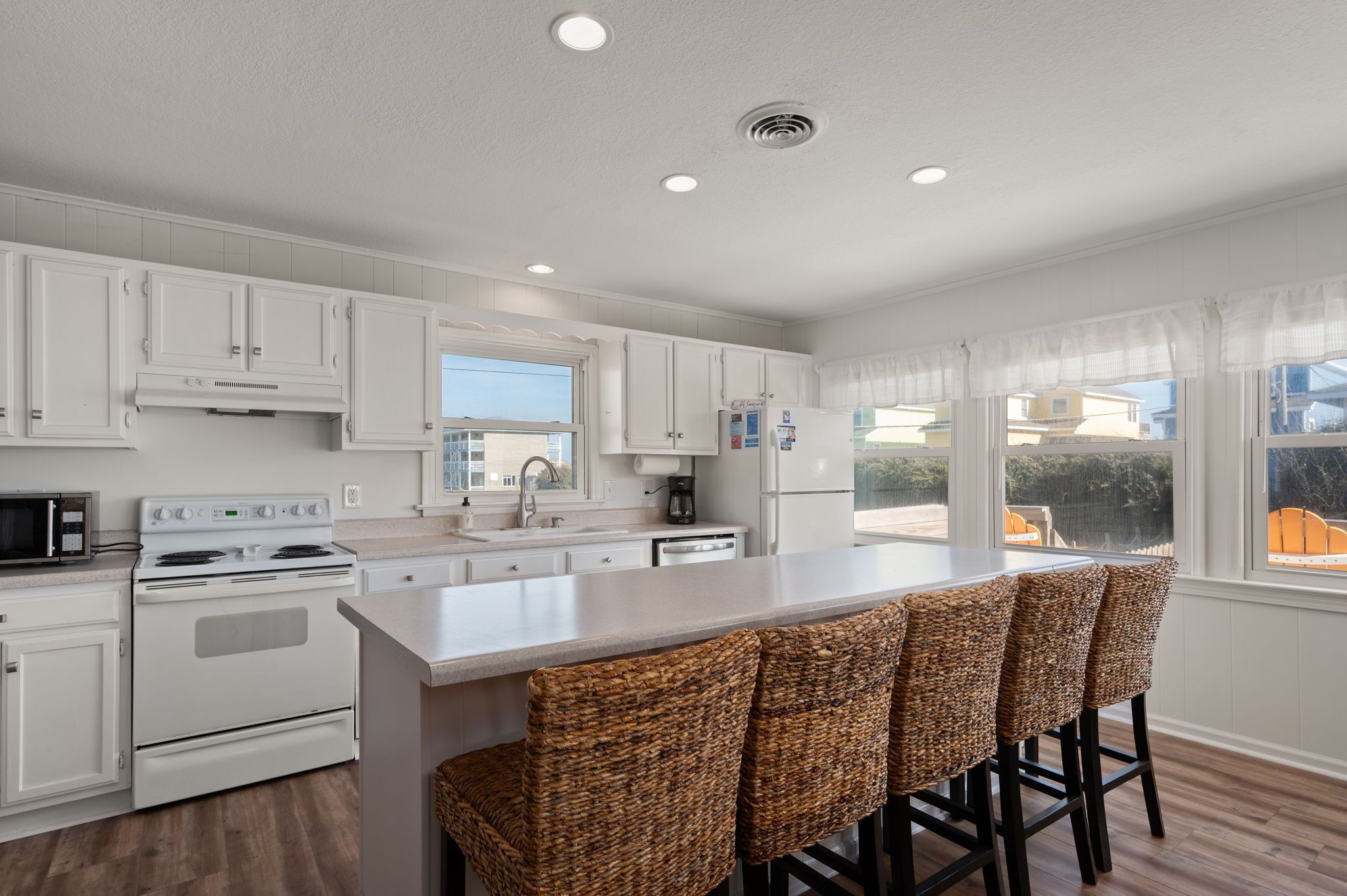 Una cocina moderna con armarios blancos, una isla central con taburetes altos, microondas, estufa y refrigerador.