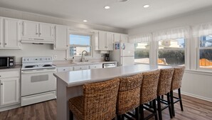 A modern kitchen with white cabinetry, a central island with bar stools, a microwave, stove, and refrigerator. - Direct Beach Access at my newly updated cottage in Nags Head, NC (Nags Head)