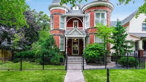A Victorian-style house with a prominent turret and bay windows, surrounded by a well-maintained lawn and a black iron fence. - The Victorian on Victoria (Windsor)