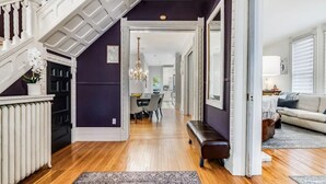 A spacious hallway with wooden flooring, a bench, and a dining area in the background. - The Victorian on Victoria (Windsor)