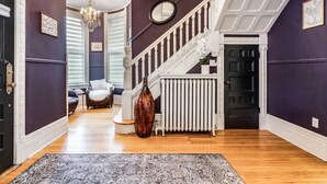 A hallway with a staircase, a radiator, a chair, and a rug. - The Victorian on Victoria (Windsor)