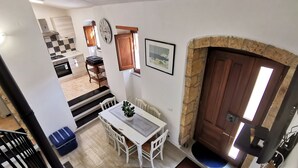 Un comedor con una mesa y sillas blancas, una planta en maceta y una cocina al fondo.