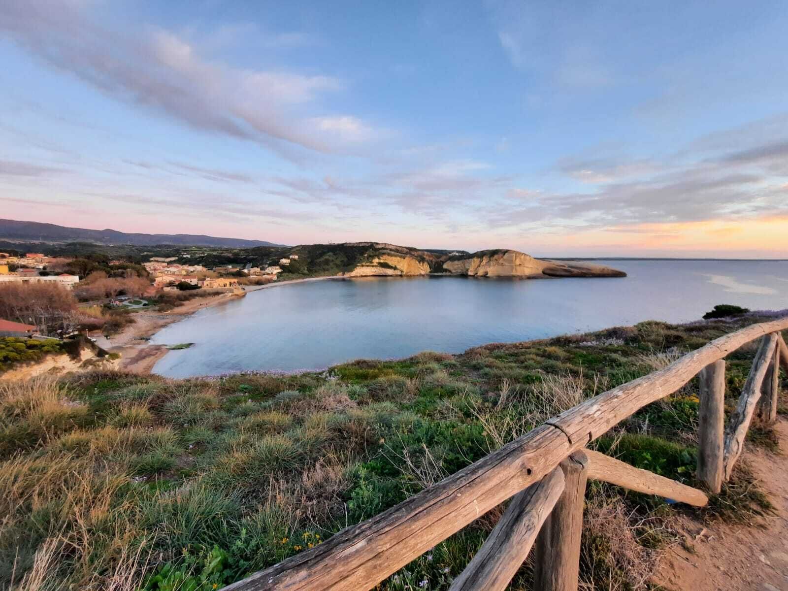 A coastal landscape with a wooden fence, a calm sea, and a town in the background.