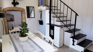 Un comedor con una mesa blanca, sillas y una planta en maceta. Una escalera con barandillas negras conduce a un nivel superior.
