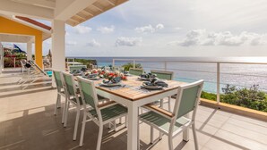 Un coin repas avec une table dressée pour quatre personnes, offrant une vue imprenable sur l’océan.