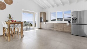 Une cuisine moderne dotée d’un grand îlot central, d’appareils électroménagers en acier inoxydable et offrant une vue sur l’extérieur.