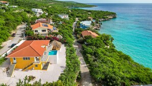 Une propriété située sur la côte, dotée d’une piscine, d’un bâtiment jaune et offrant une vue sur la mer.