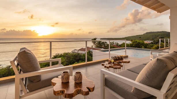 Une terrasse offrant une vue sur le coucher de soleil sur la mer, une piscine et des espaces de détente en plein air.