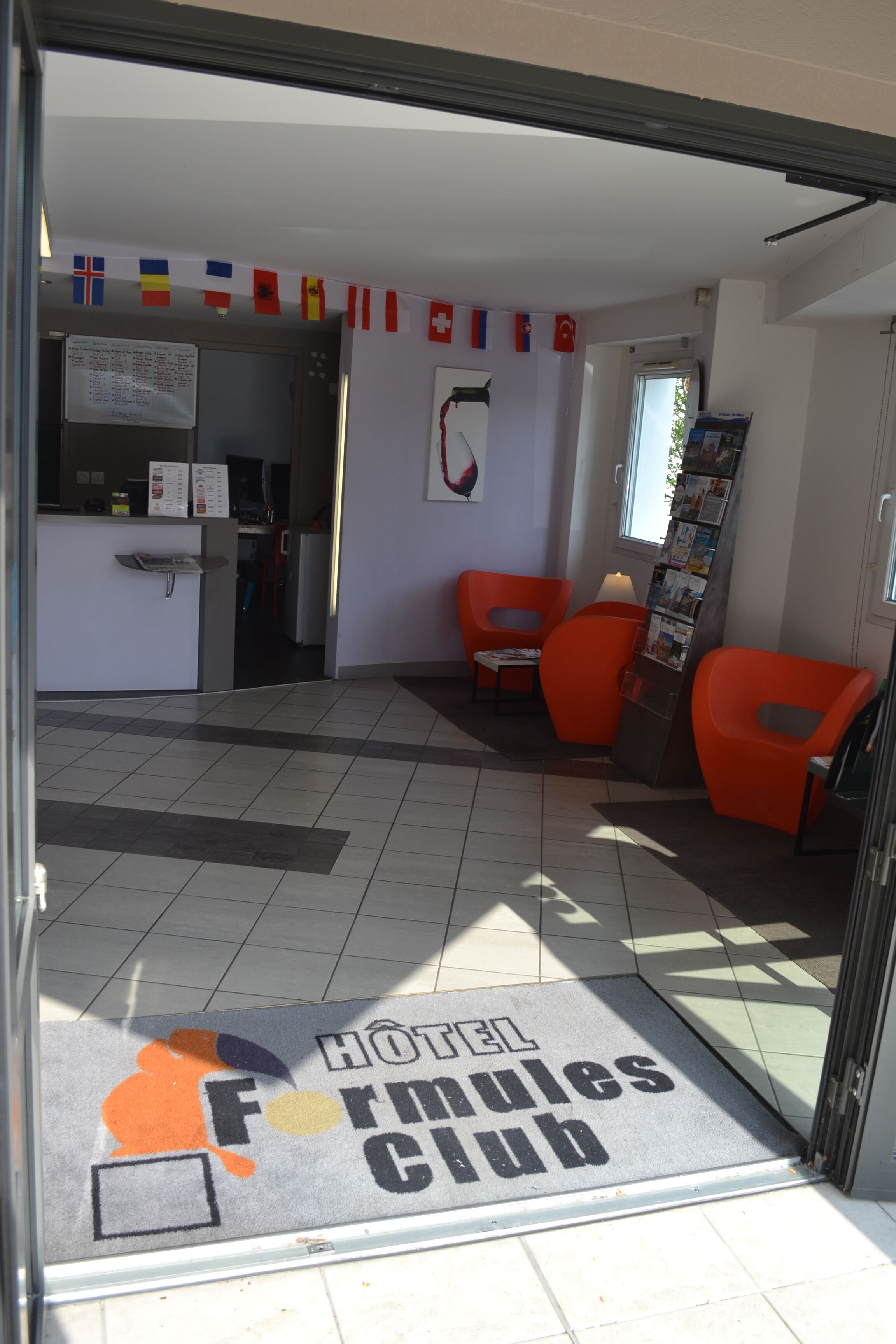 A hotel lobby with a reception desk, a bulletin board, and orange seating areas.