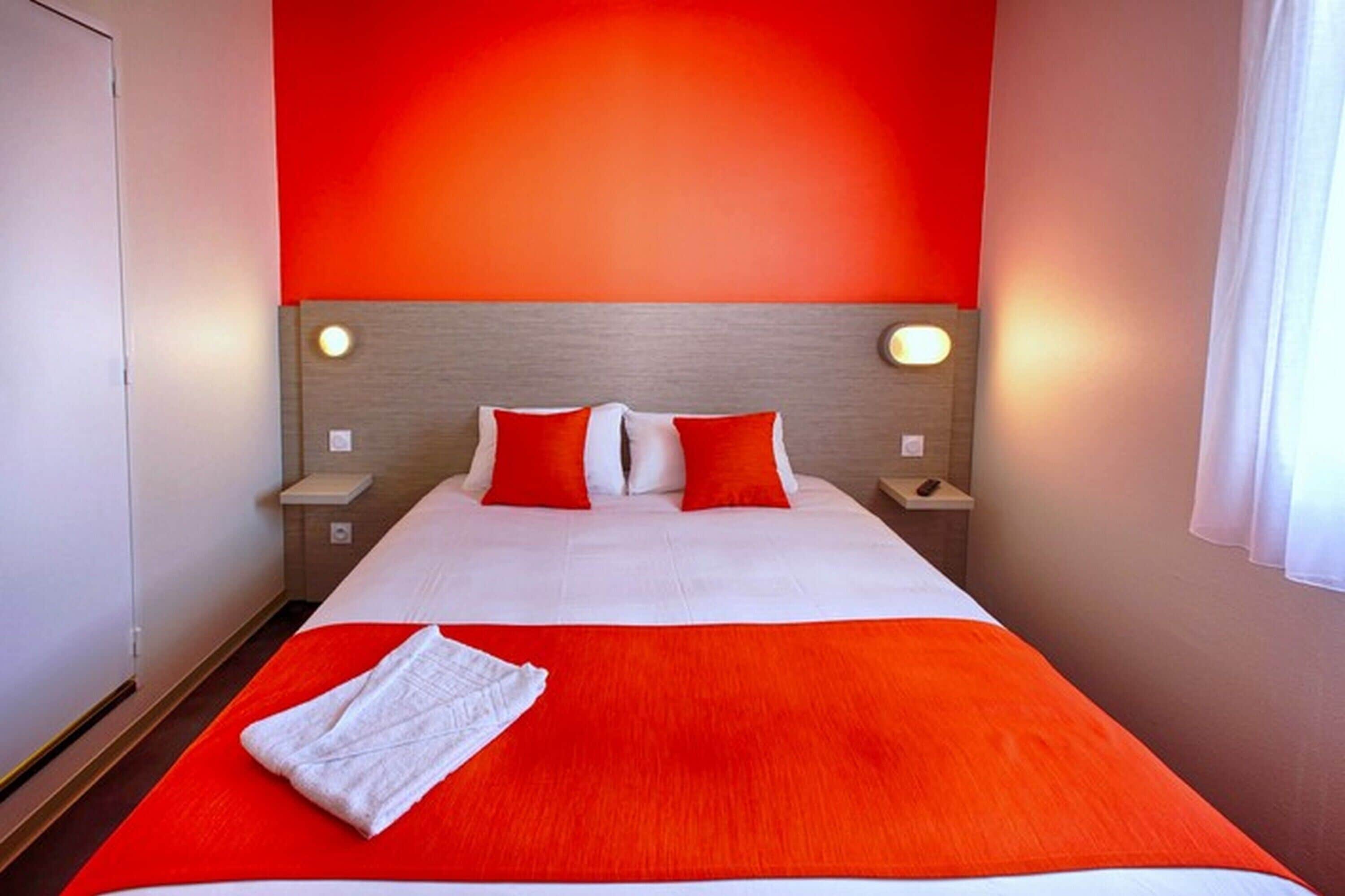A hotel room with a large bed, red bedding, and two bedside lamps.