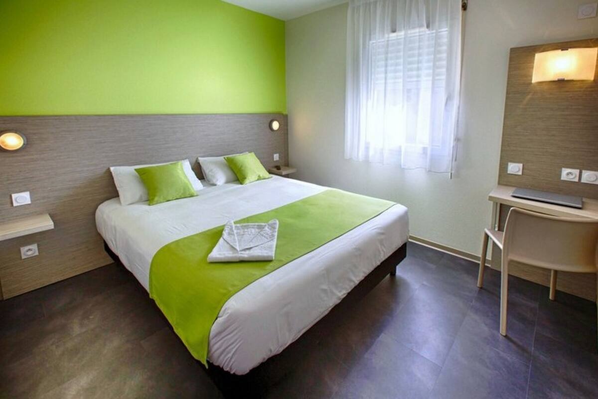 Une chambre d’hôtel moderne avec un grand lit, des touches de vert, une table de chevet, une chaise et un miroir.