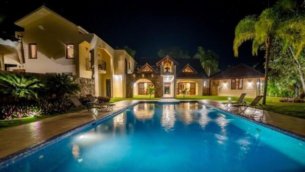 A large, well-lit swimming pool with lounge chairs, surrounded by a landscaped garden and a multi-story building with a central arched entrance. - Casa Las Brisas – Caribbean Vacation Rental (Cabarete)