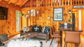 A cozy cabin interior with wooden walls, a sofa, a coffee table, and a bar area.