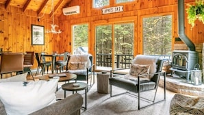 A cozy wooden cabin interior with a fireplace, large windows, and a sign reading "APRES SKI".