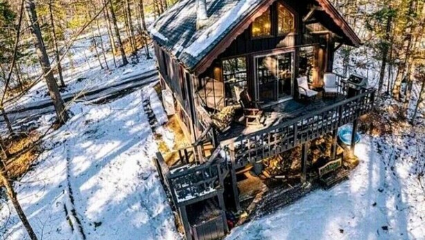 A cabin with a deck, surrounded by snow-covered ground and trees.