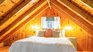 A cozy attic bedroom with a sloped wooden ceiling, a bed with white bedding, and two bedside lamps.
