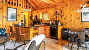 A wooden cabin interior with a kitchen, dining area, and bar.