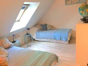A cozy attic bedroom with a sloped ceiling, a skylight, a bed with a blue blanket, a small table with a lamp, and a globe on a shelf.
