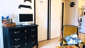 A room with a black dresser, a white door labeled "CHAMBRE", a chair with a patterned cushion, and a small table with a board game.