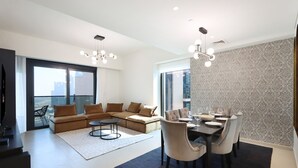 A modern living room with a sectional sofa, a dining table set for six, and a large window offering a city view. - Livbnb - 3BR + 1 with Burj and Fountain Views (Dubai)