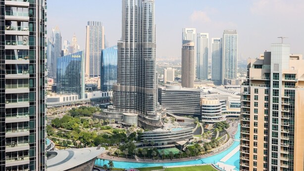A high-rise building with a curved facade, surrounded by other modern skyscrapers, a landscaped area with a pool, and a clear sky. - Livbnb - 3BR + 1 with Burj and Fountain Views (Dubai)