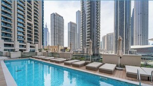 A rooftop pool with lounge chairs and umbrellas, surrounded by high-rise buildings. - Livbnb - 3BR + 1 with Burj and Fountain Views (Dubai)