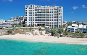 Um hotel à beira-mar com vários andares, varandas e uma praia arenosa em primeiro plano.