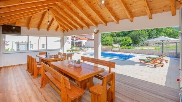 Une terrasse en bois avec une piscine, un espace salon extérieur et un coin abrité comprenant une table et des bancs.