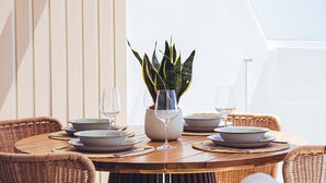 A round wooden table set for dining with wicker chairs, a potted plant, and wine glasses.