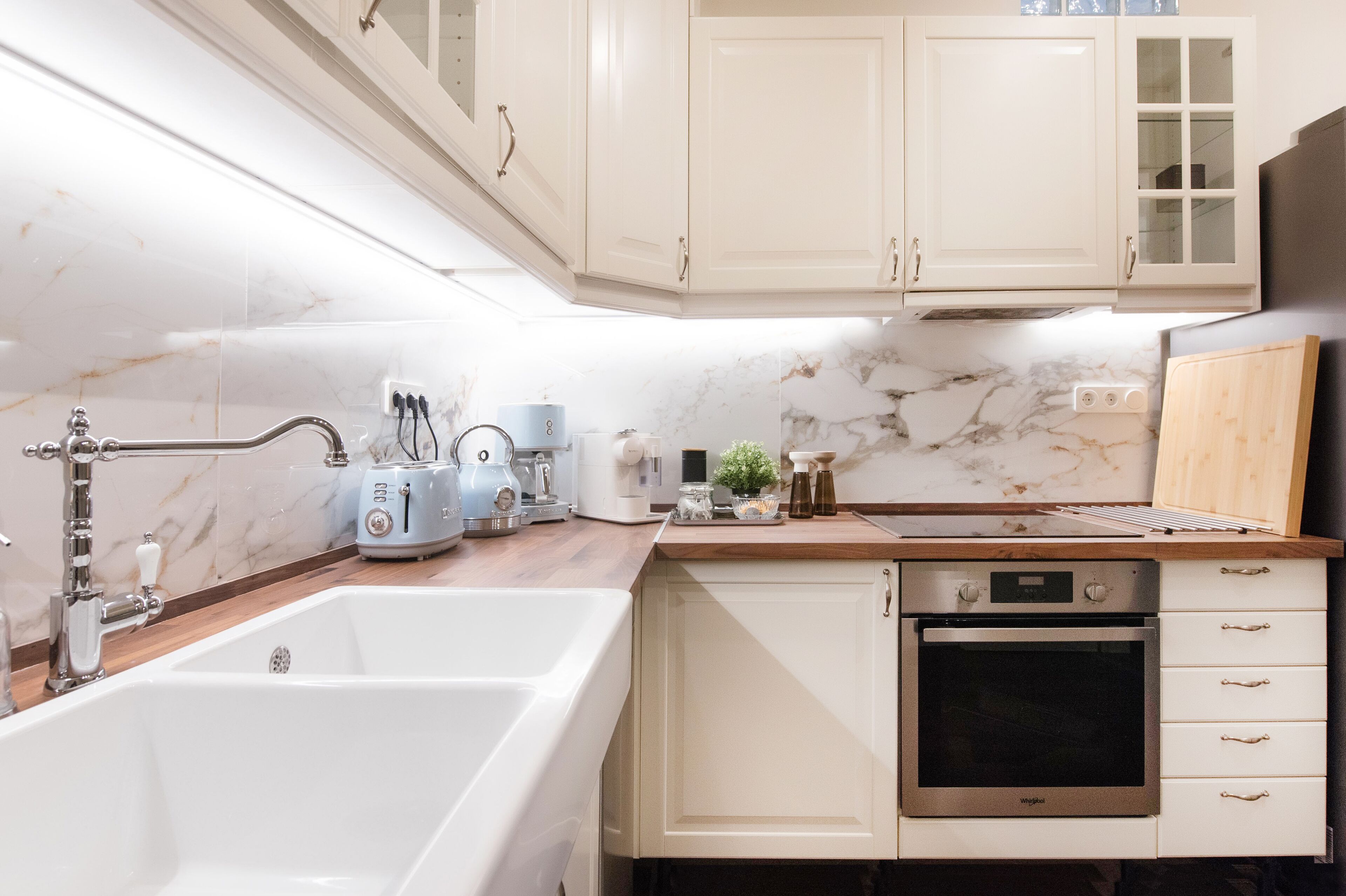 A kitchen with white cabinets, a built-in oven, a sink, and a countertop with various appliances.