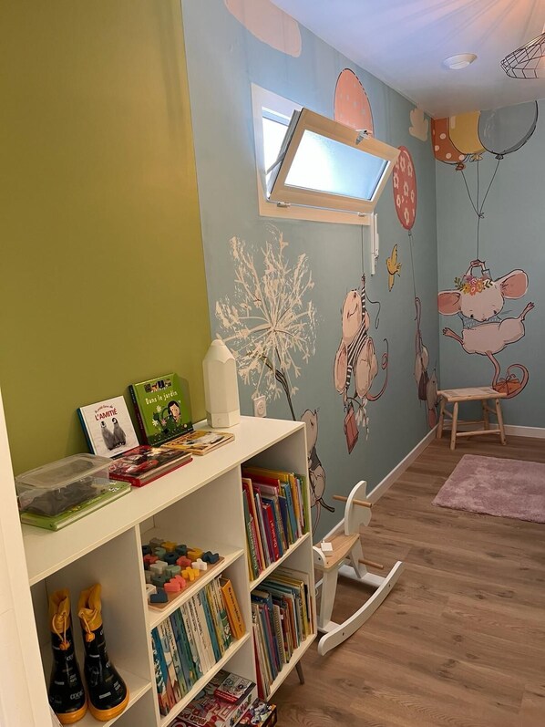 Una habitación infantil con una estantería, un sillón mecedora y un mural en la pared.