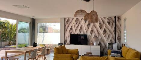 Una sala de estar moderna con un televisor grande, sofás amarillos y una zona de comedor con muebles de madera.