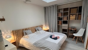 Une chambre moderne avec une lucarne, un lit avec une literie à rayures, une table de chevet avec une lampe, une chaise et une bibliothèque intégrée.