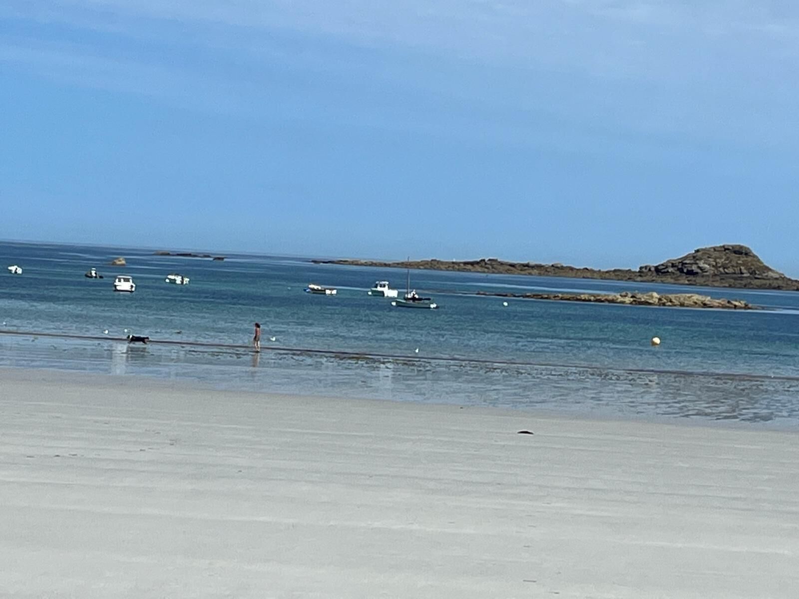 Una playa con barcos y una isla rocosa a lo lejos.