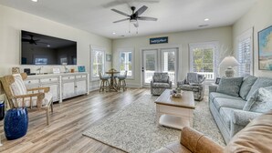 A spacious living room with a ceiling fan, a dining area with a table and chairs, and a kitchen area with a large window. - Luxurious 5 Bedroom, 5.5 Bath with Private Pool & Elevator (Garden City Beach)