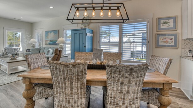 A dining area with a wooden table and wicker chairs, a blue cabinet, and a hanging light fixture. - Luxurious 5 Bedroom, 5.5 Bath with Private Pool & Elevator (Garden City Beach)