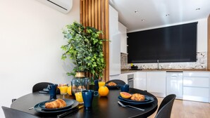 Moderni ruokailutila, jossa on pyöreä pöytä, tuoleja, ruukkukasvi sekä aamiaistarvikkeita, kuten croissantteja ja appelsiinimehua.