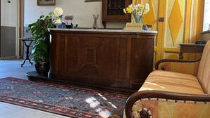A reception area with a wooden desk, a sofa, a patterned rug, and a cabinet with glass doors. - Dimora San Secondo (San Secondo di Pinerolo)