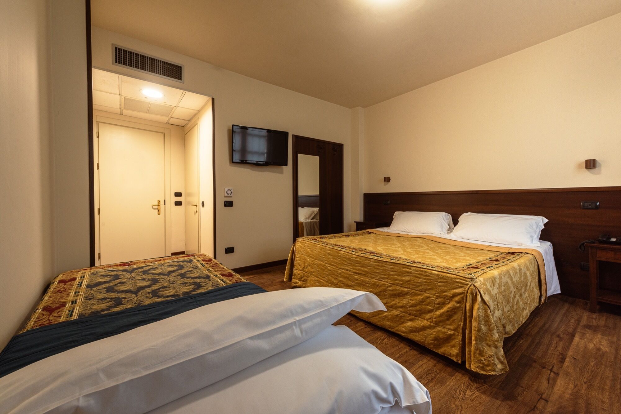 Habitación de hotel con dos camas, un televisor montado en la pared y un cabecero de madera.