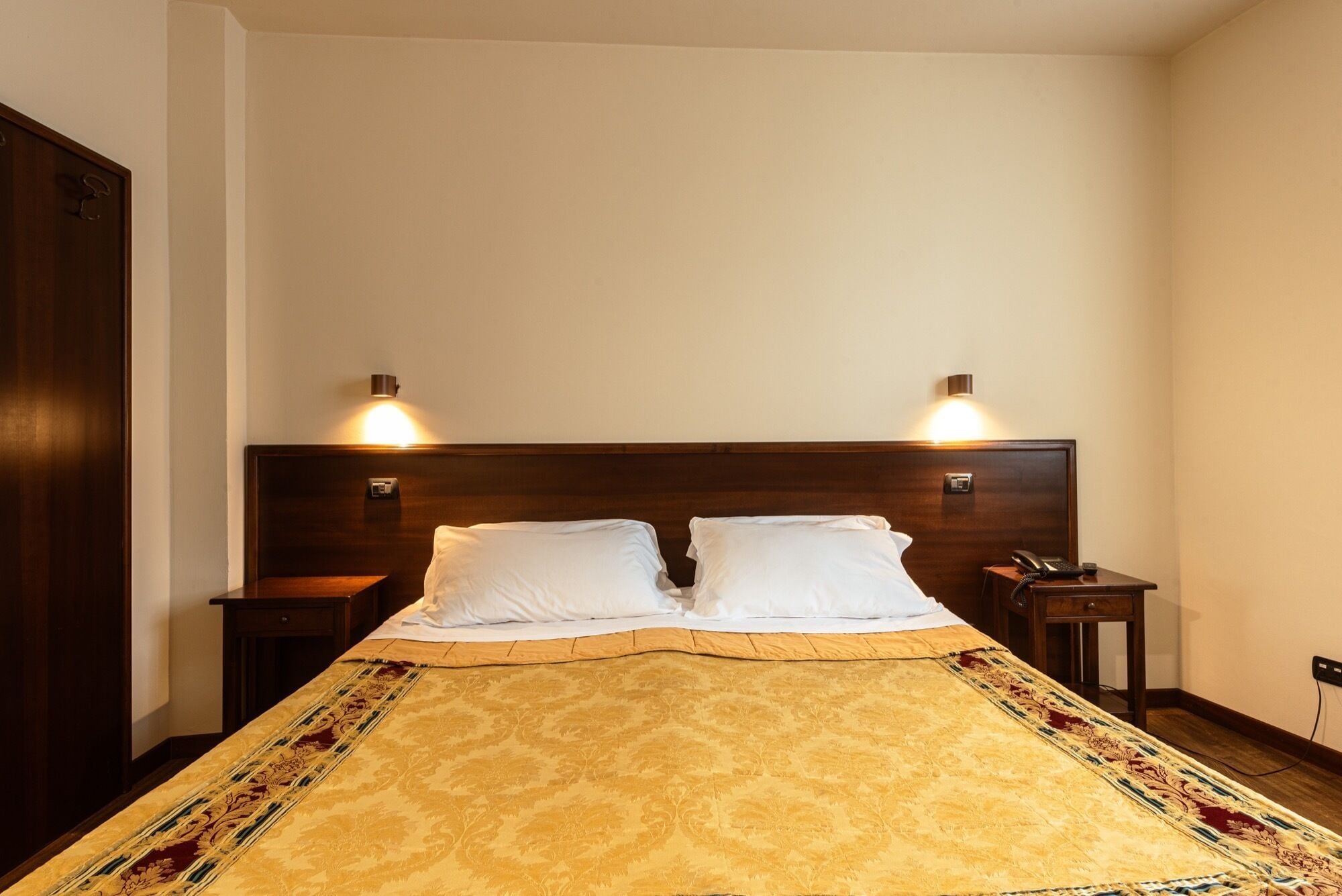 A hotel room with a large bed, two bedside tables, a wooden headboard, and wall-mounted lamps.