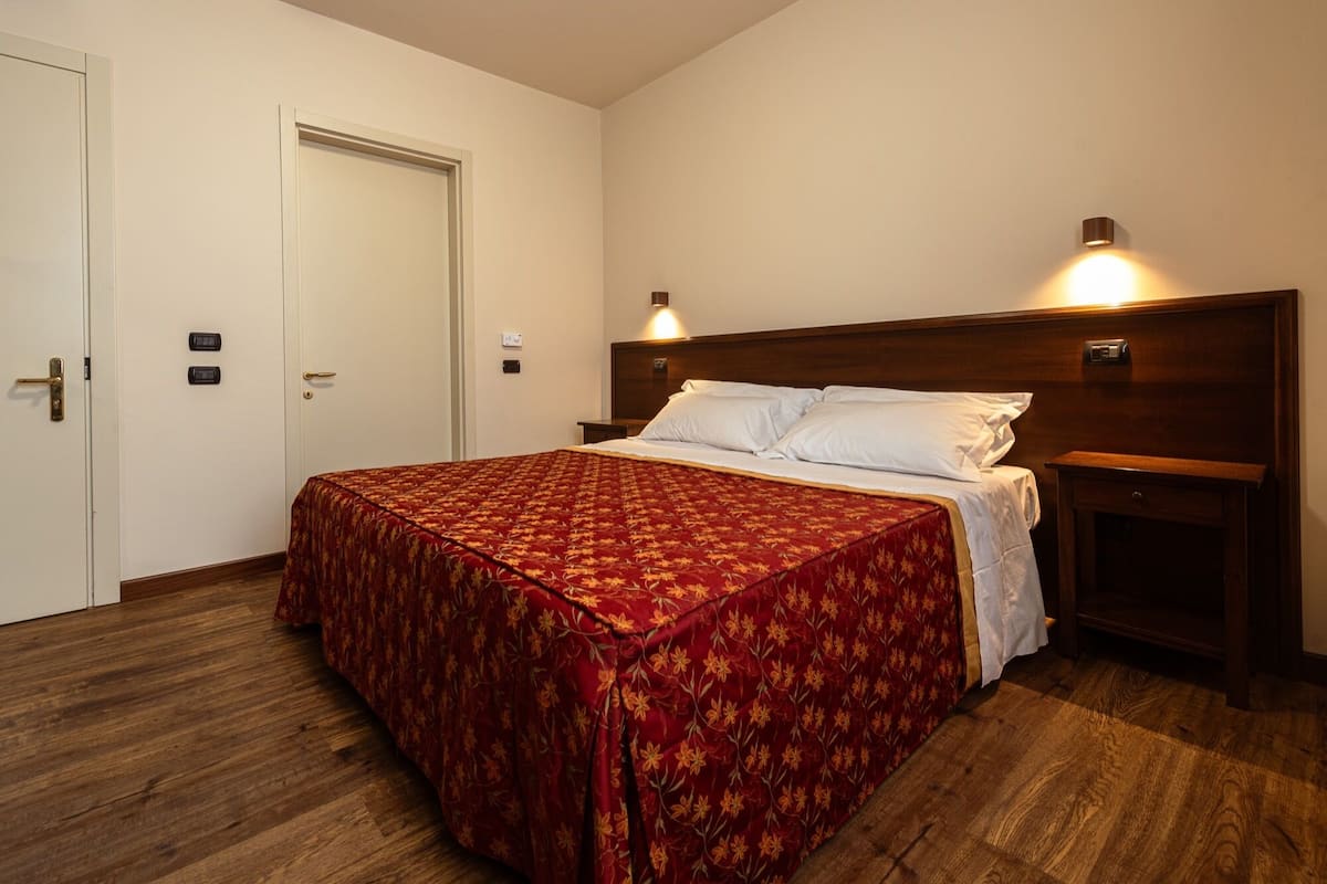 A hotel room with a large bed, wooden headboard, two bedside tables, and a door with a handle.