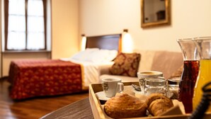A hotel room with a bed, a bedside table with a tray of pastries, a cup of coffee, and a glass of tea. - Dimora San Secondo (San Secondo di Pinerolo)