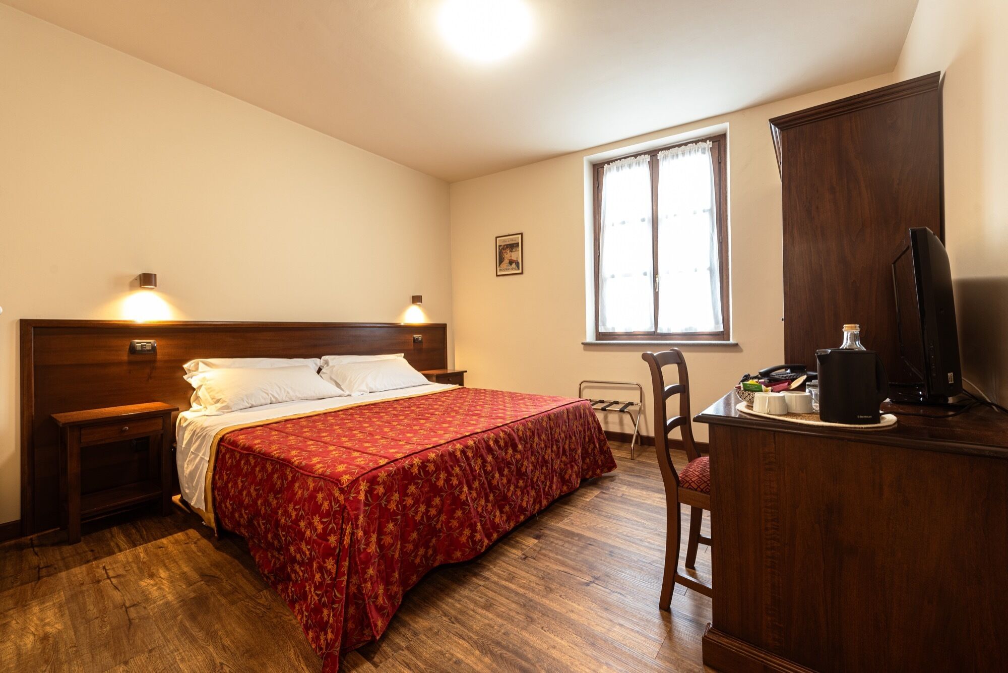 A hotel room with a wooden bed, a desk with a computer, a chair, and a window with curtains.