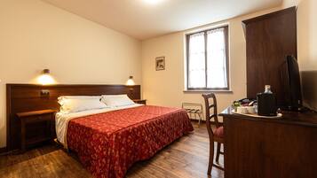A hotel room with a wooden bed, a desk with a computer, a chair, and a window with curtains.